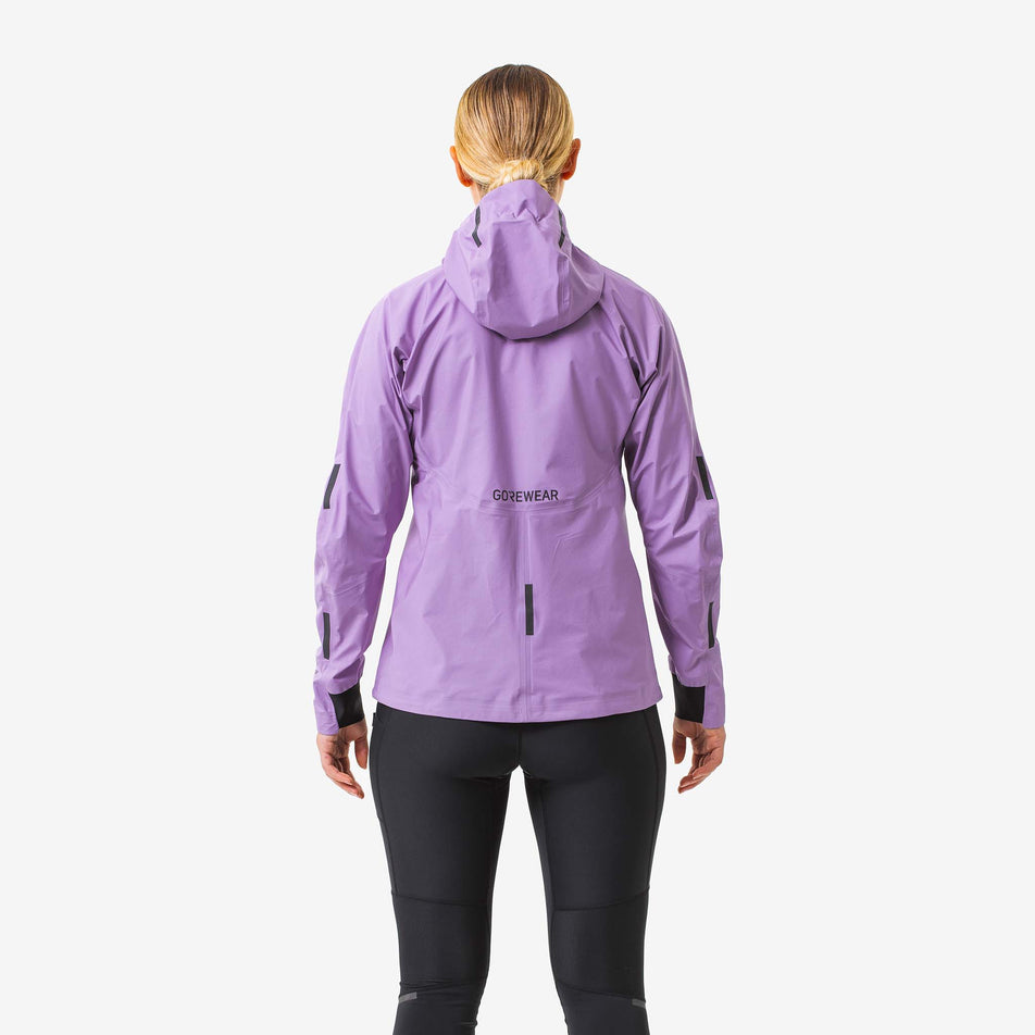 Back view of a model wearing a GOREWEAR Women's Concurve GORE-TEX Jacket in the Scrub Purple colourway. Model is also wearing leggings. (8177157079202)