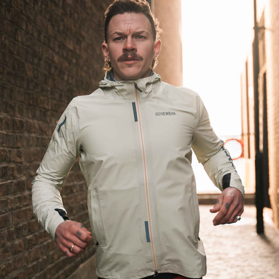A model running in the GOREWEAR Men's Concurve GORE-TEX Logo Jacket in the Tech Beige/Black colourway. (8751737962658)