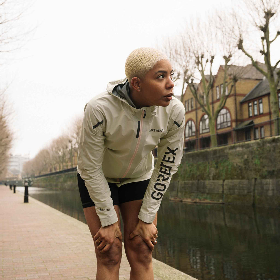 Front view of a model wearing the GOREWEAR Women's Concurve GORE-TEX Logo Jacket in the Tech Beige/Black colourway. (8752081207458)