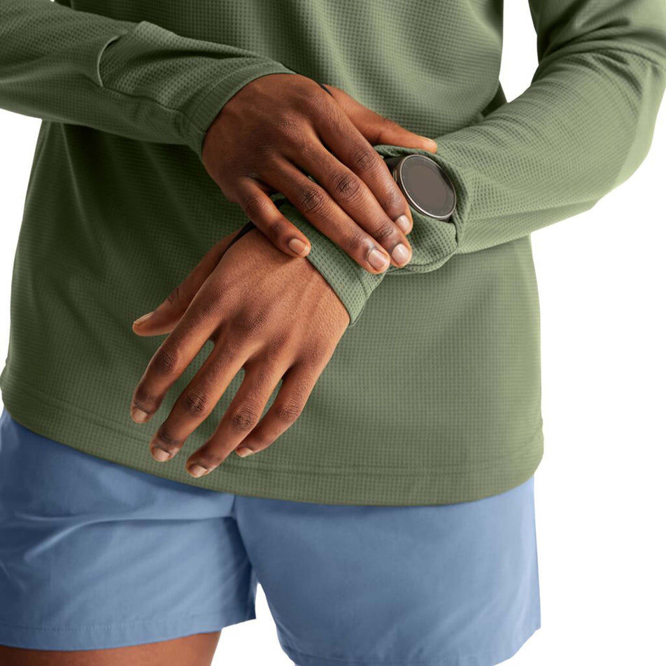 Close-up view of a model wearing an On Men's Climate Shirt in the Taiqa colourway. Model is demonstrating that a running watch can show through a 'watch window' gap in the cuff of the sleeve.  (8005080088738)