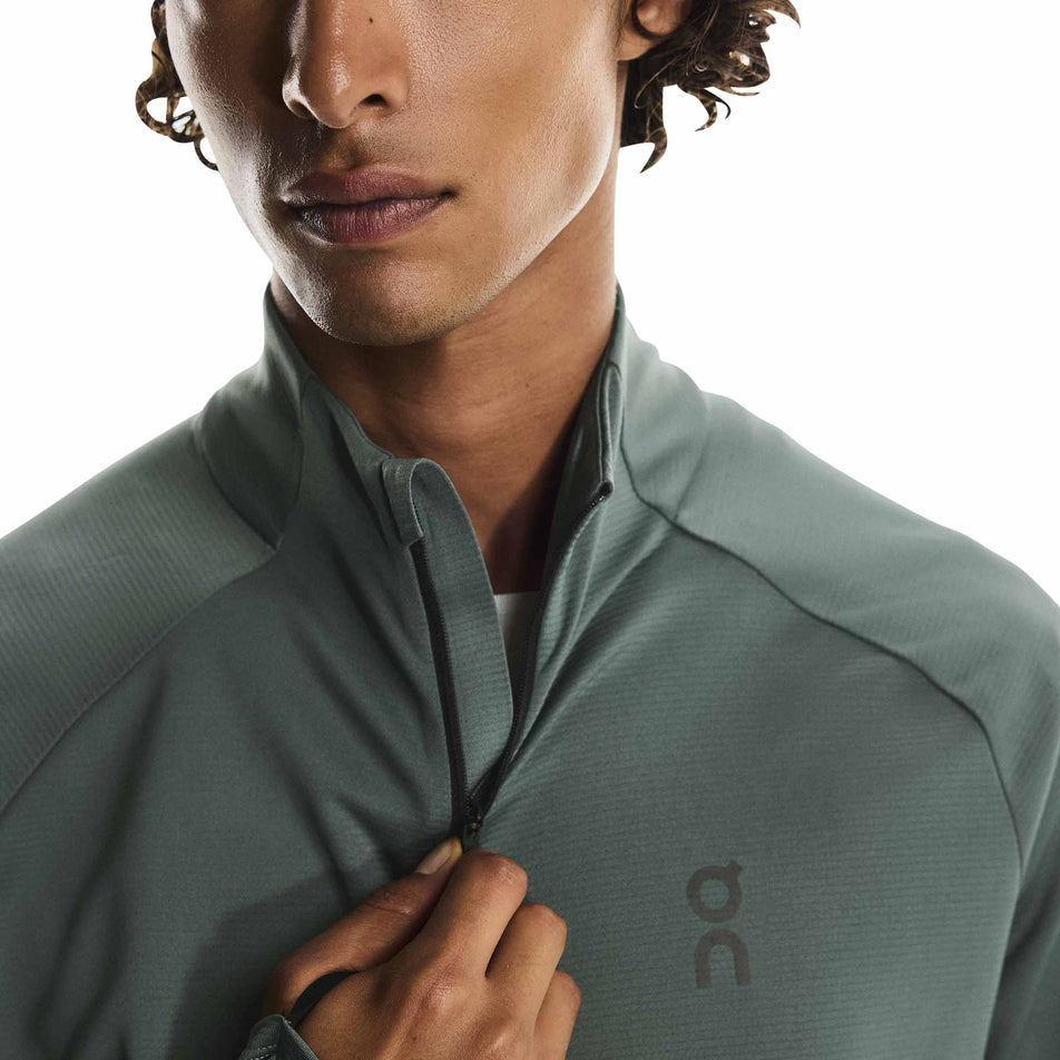 A model adjusting the 1/2 zip on the On Men's Climate Shirt in the Olive colourway. (8790094643362)