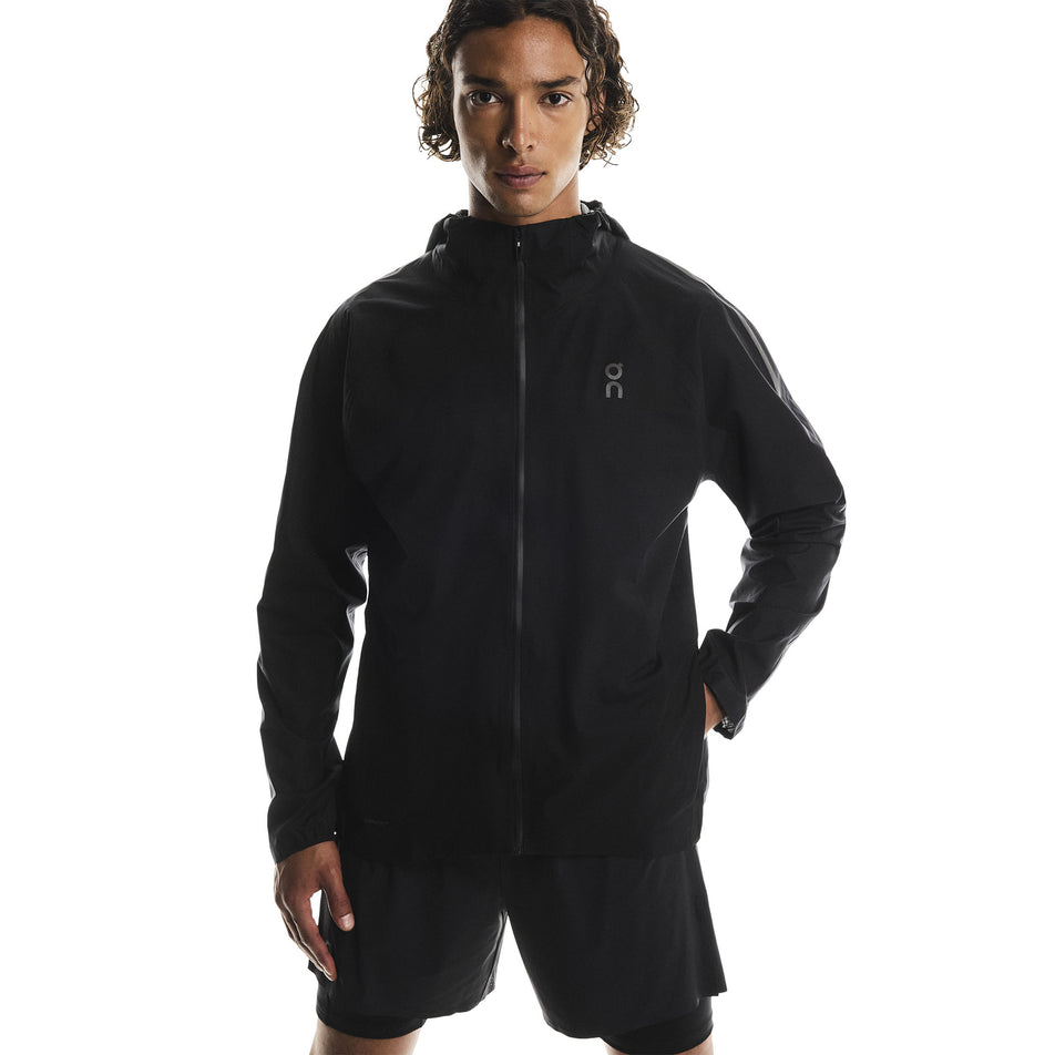 Front view of a model wearing the On Men's Performance Waterproof Jacket in the Black colourway. (8790101819554)