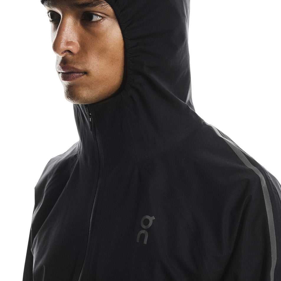 Angled view of a model wearing the On Men's Performance Waterproof Jacket in the Black colourway. (8790101819554)