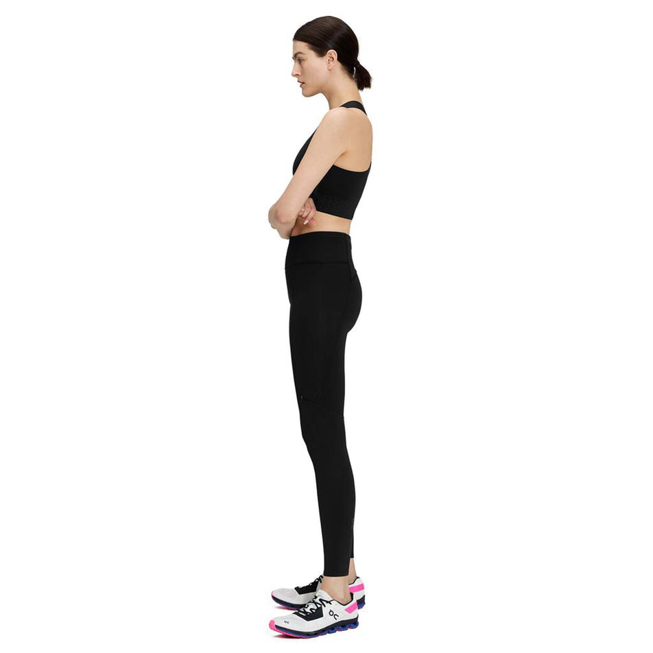 Side view of a model wearing a pair of On Women's Performance Tights in the black colourway (8002755264674)