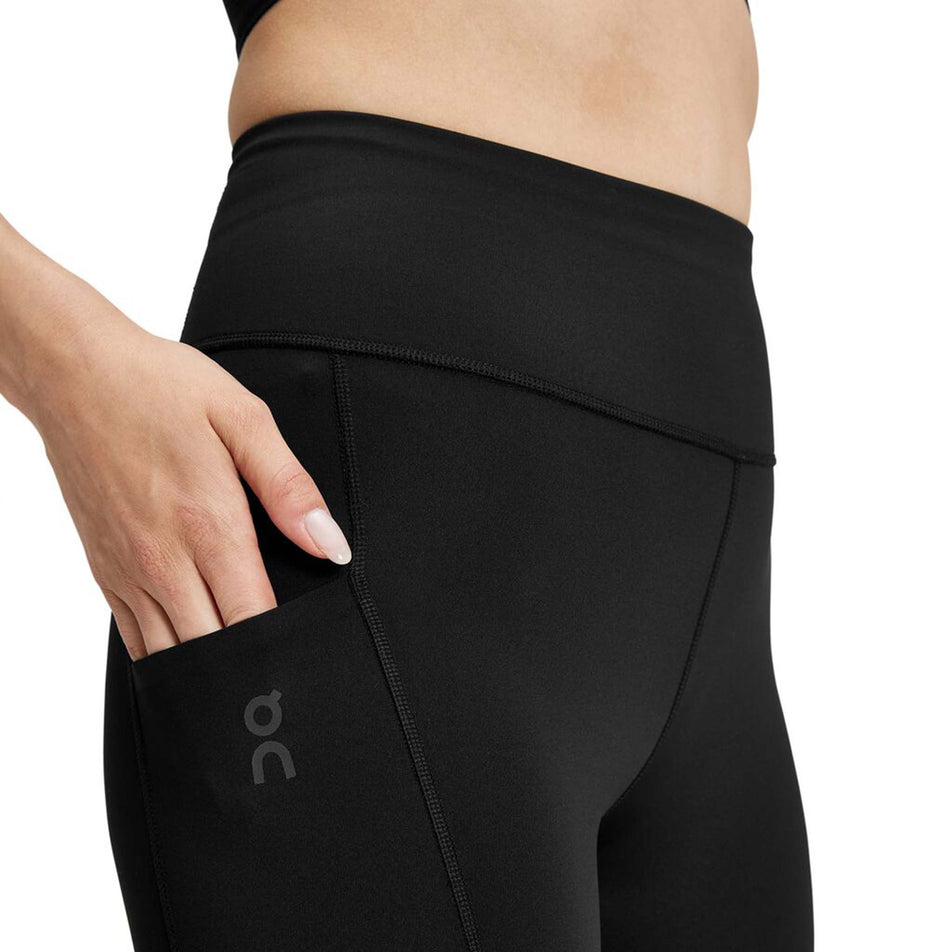 Close-up side view of a model wearing a pair of On Women's Performance Tights in the black colourway. Upper third of the tights is visible. Model demonstrating that there is a pocket on the right side of the thigh area.  (8002755264674)