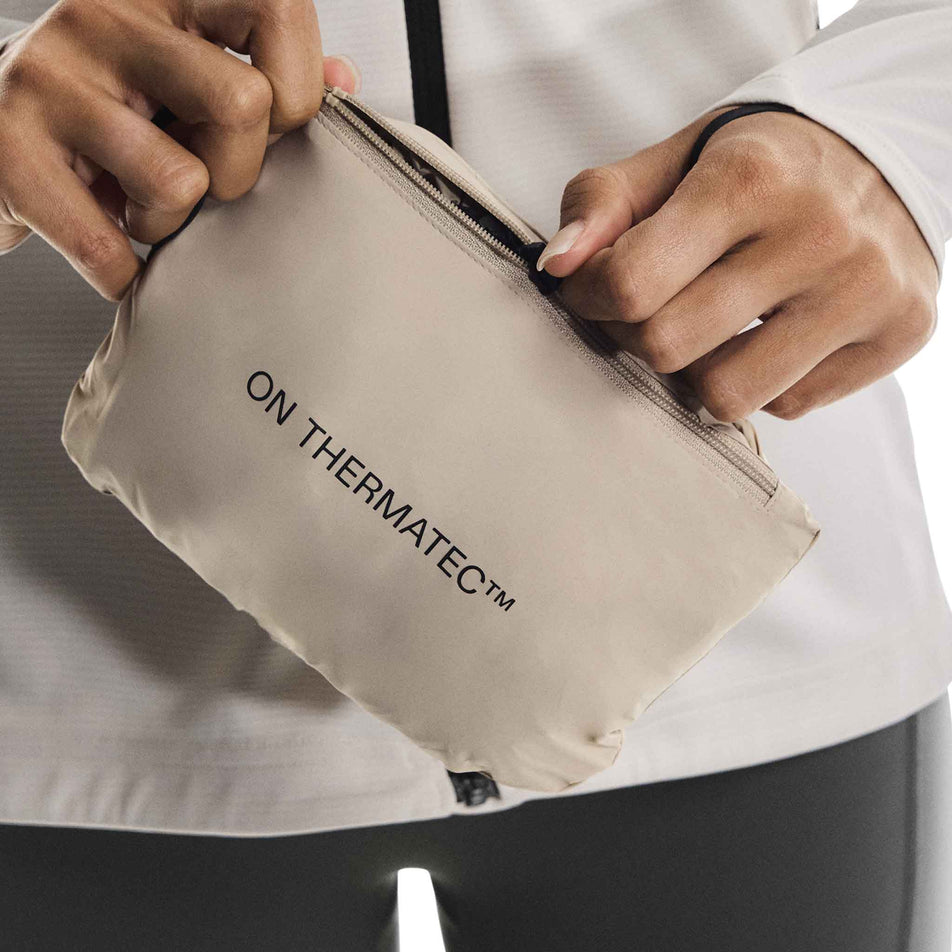 The On Women's Weather Vest in the Desert/Eclipse colourway folded up into its pocket. (8790011412642)