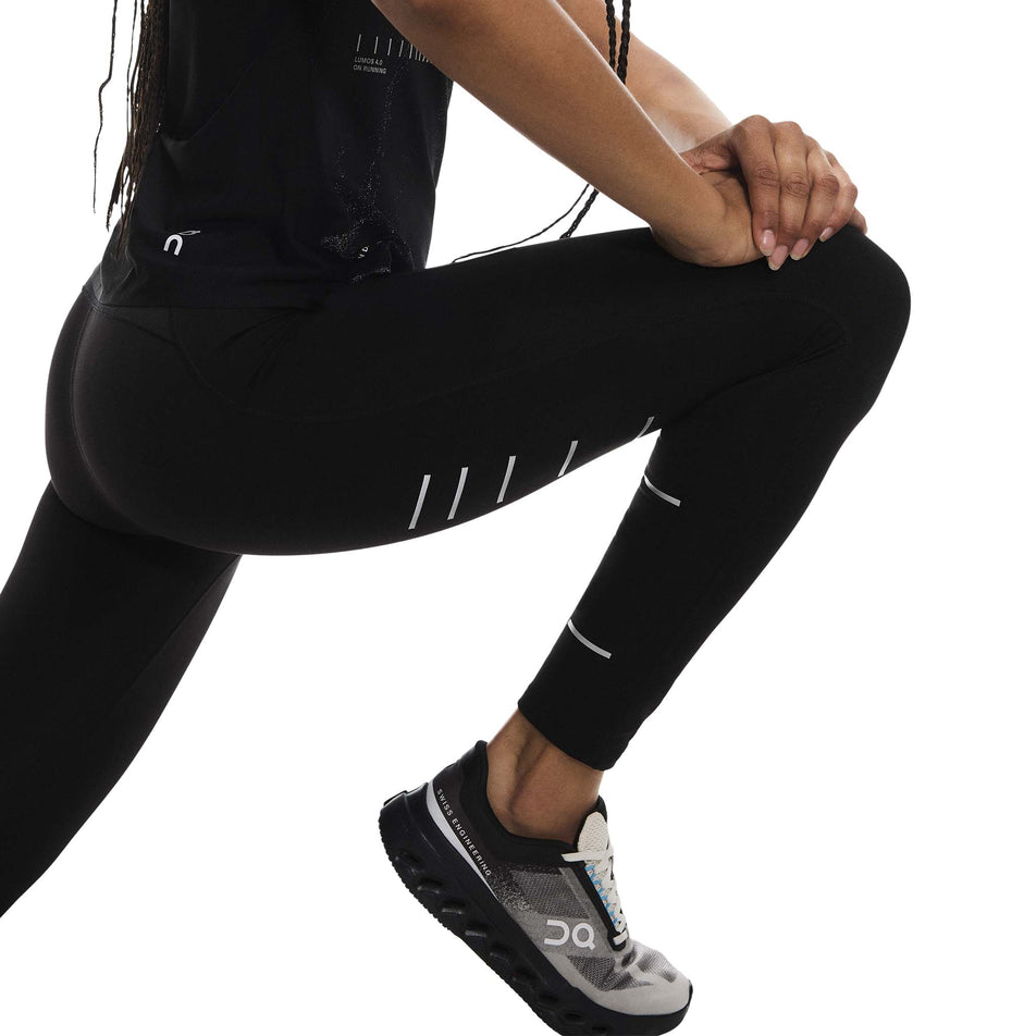 Side view of a model wearing the On Women's Performance Tights Lumos in the Black colourway. (8790043394210)