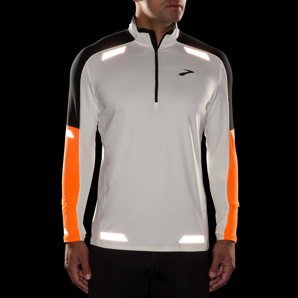 Front view of a model wearing the Brooks Men's Run Visible 1/2 Zip 2.0 in the Ecru/Fluoro Flash/Black colourway. Reflective strips are reflecting artificial light. (8499413188770)