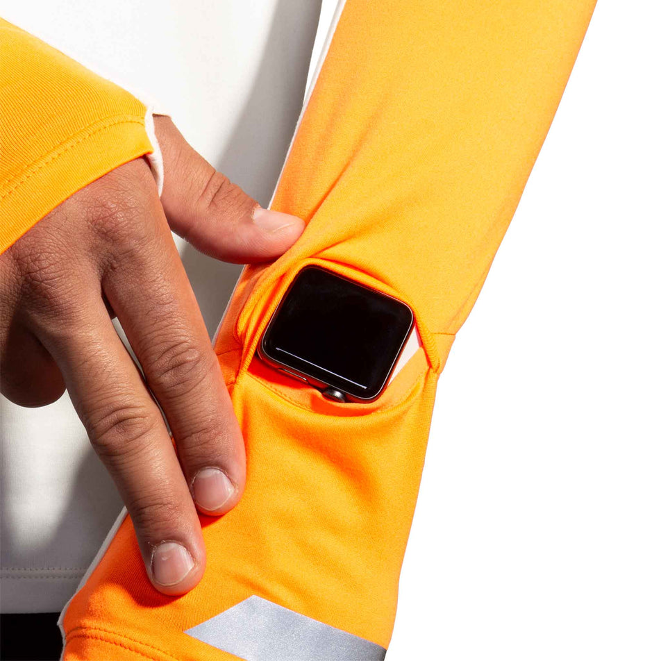 The watch window on the left sleeve of the Brooks Men's Run Visible 1/2 Zip 2.0 in the Ecru/Fluoro Flash/Black colourway. (8499413188770)