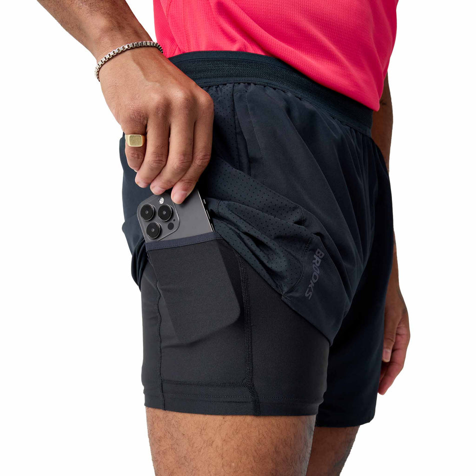 A model demonstrating the stash pocket on the side of the Brooks Men's Dash 2-in-1 Shorts in the Black colourway.