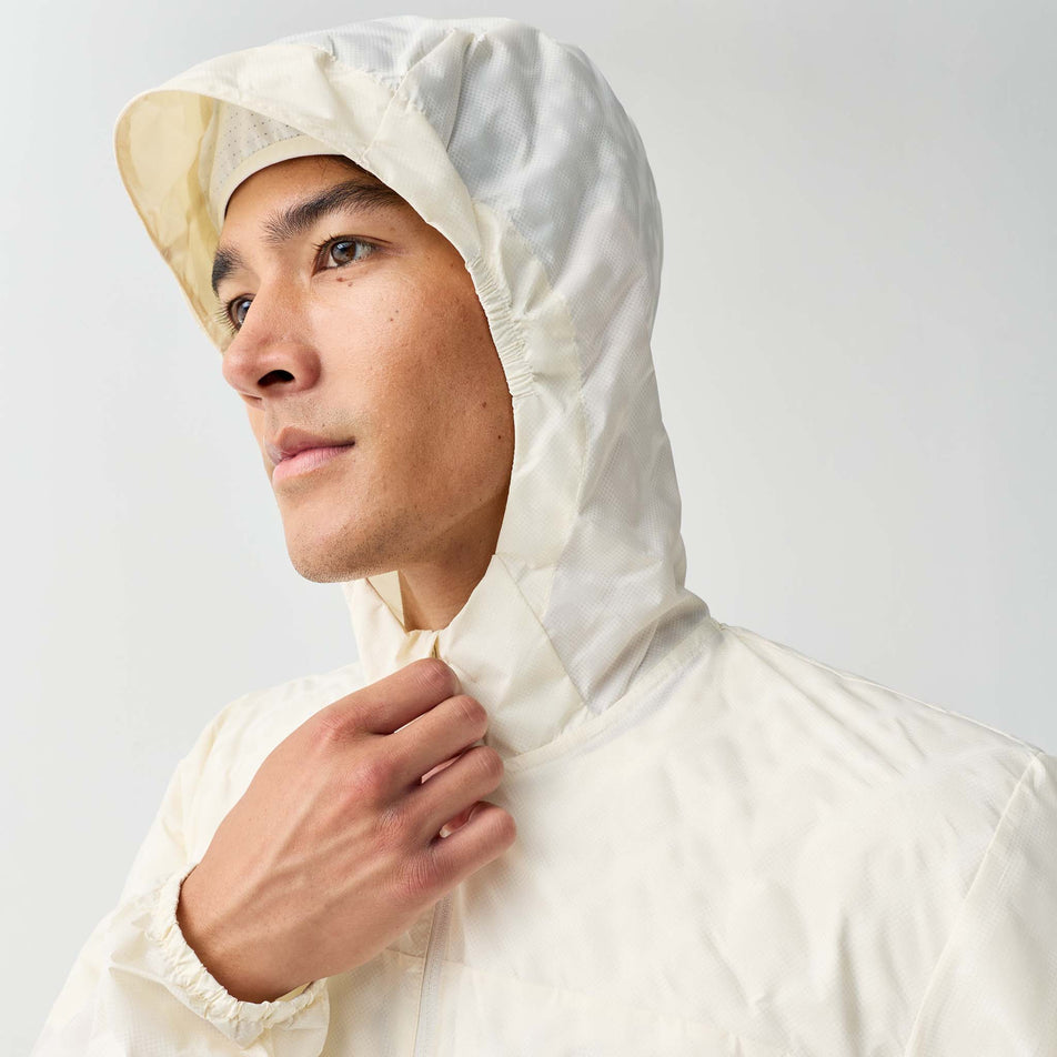 Angled view of a model wearing the Brooks Men's Canopy Reflective Jacket in the Reflective Wordmark Bone colourway.