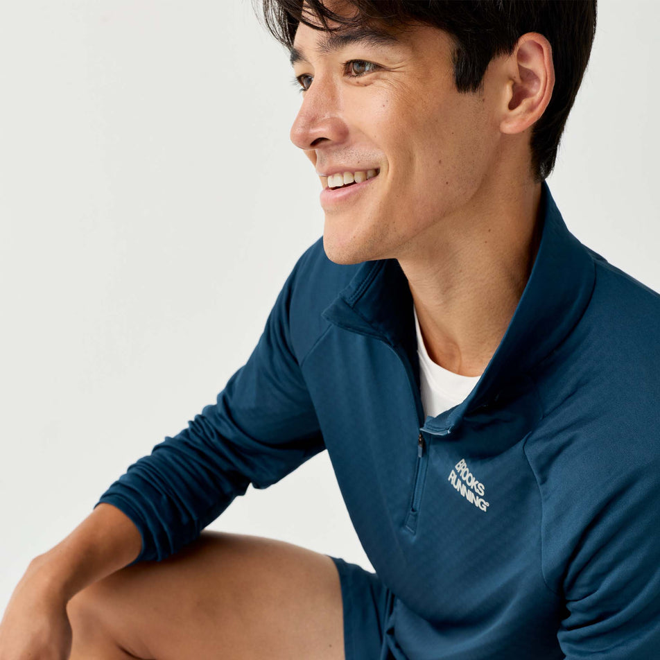 Angled view of a model wearing the Brooks Men's Thermal Reflective 1/2 Zip in the Reflective Wordmark Indigo colourway.