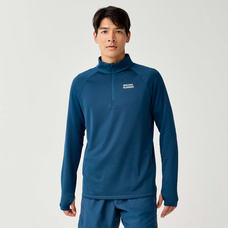 Front view of a model wearing the Brooks Men's Thermal Reflective 1/2 Zip in the Reflective Wordmark Indigo colourway.