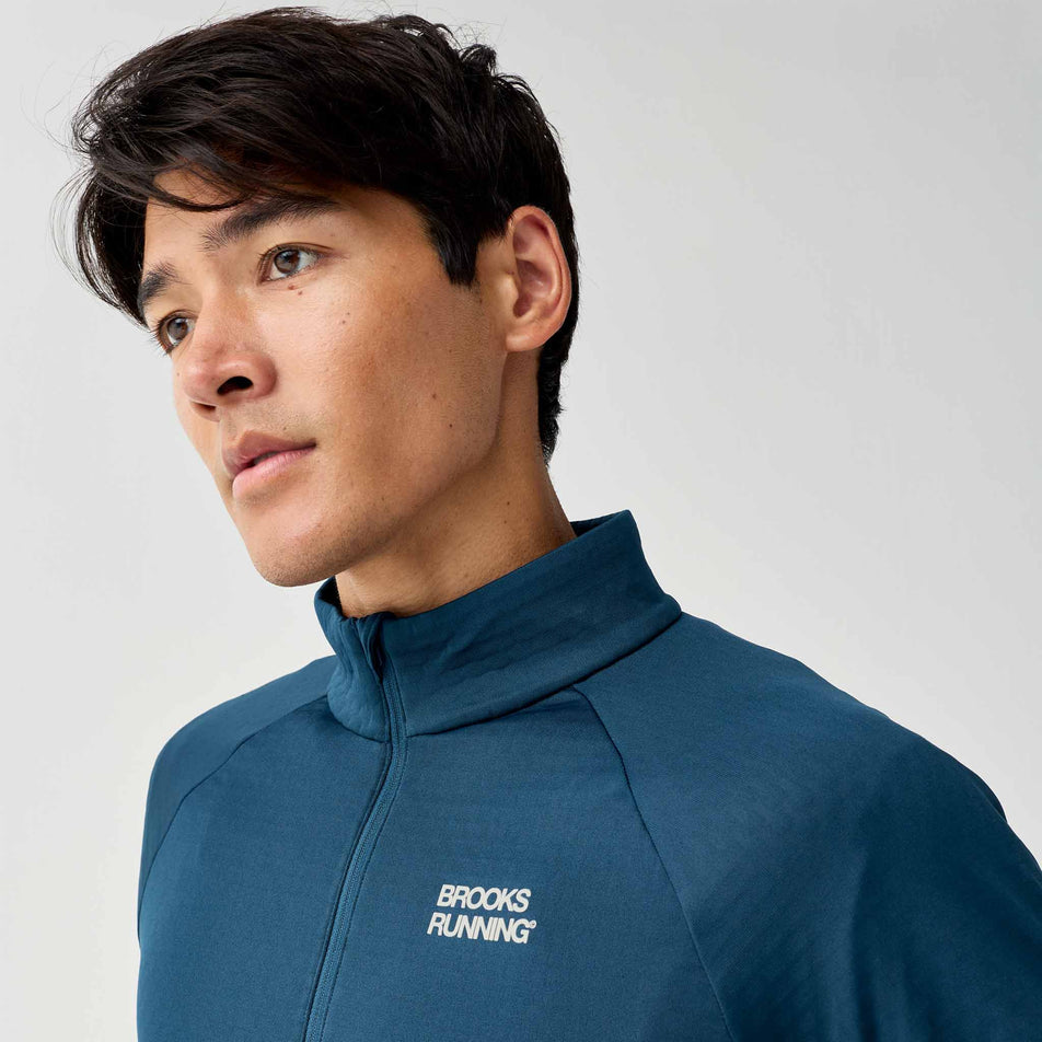 Angled view of a model wearing the Brooks Men's Thermal Reflective 1/2 Zip in the Reflective Wordmark Indigo colourway.