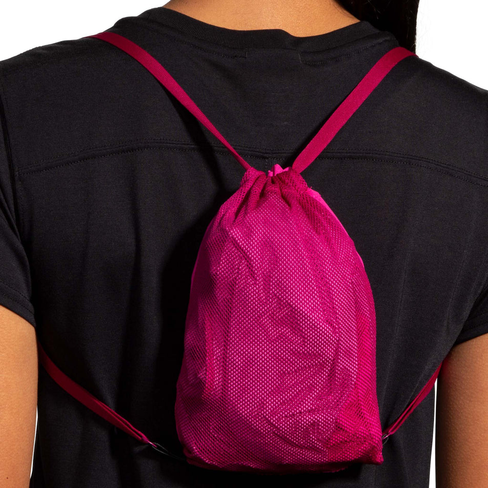 Close-up back view of a model demonstrating that a Brooks Women's Canopy Jacket, in the Frosted Mauve/Mauve colourway, can be packed into one of its pockets and worn like a backpack. (8007491748002)