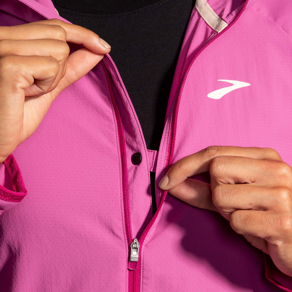 Close-up front view of a model wearing a Brooks Women's Canopy Jacket in the Frosted Mauve/Mauve colourway, demonstrating that the two sides of the jacket can be clipped shut at the chest section when the jacket is unzipped.  (8007491748002)