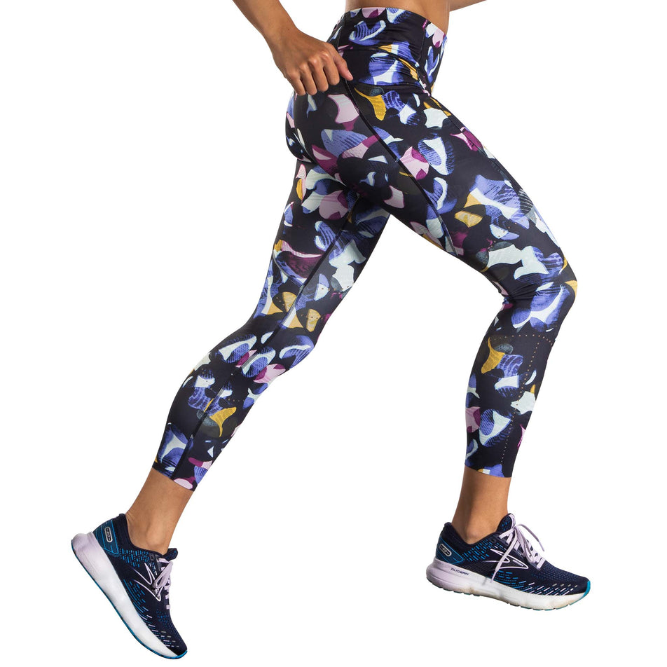 Right-lateral view of a model, in a running pose, wearing a pair of Brooks Women's 7/8 Tights in the Fast Floral Print colourway (8007499481250)