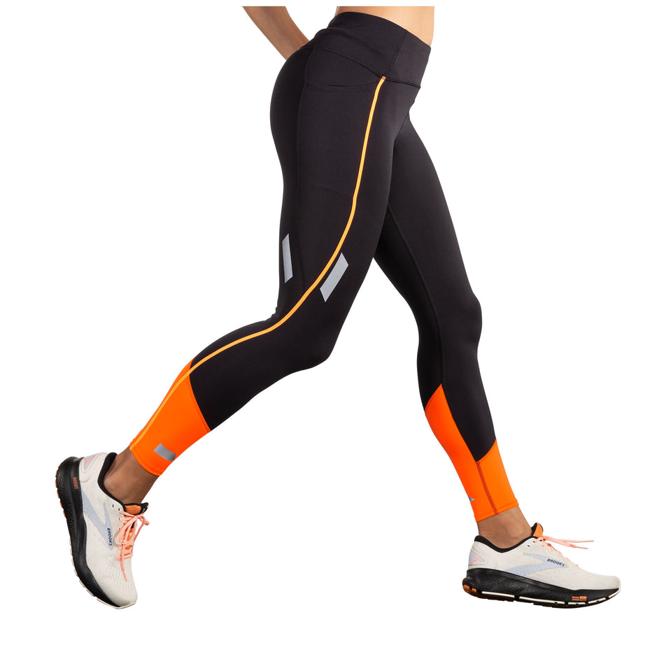 Lateral view of a model wearing the Brooks Women's Run Visible Tight 2.0 in the Black/Fluoro Flash colourway. Model is also wearing Brooks shoes. (8499453362338)