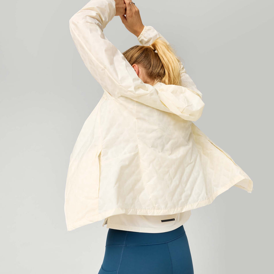 Back view of a model wearing the Brooks Women's Canopy Reflective Jacket in the Reflective Wordmark Bone colourway.
