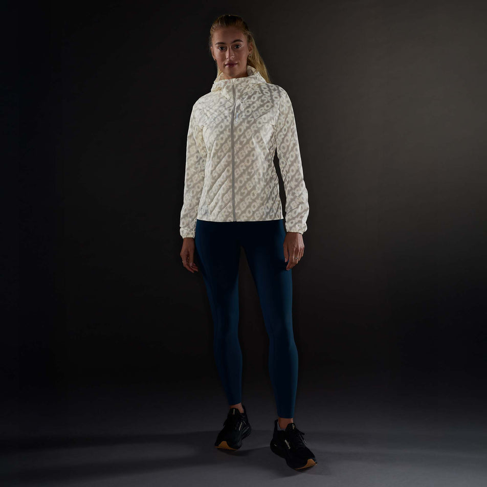 Front view of a model wearing the Brooks Women's Canopy Reflective Jacket in the Reflective Wordmark Bone colourway.