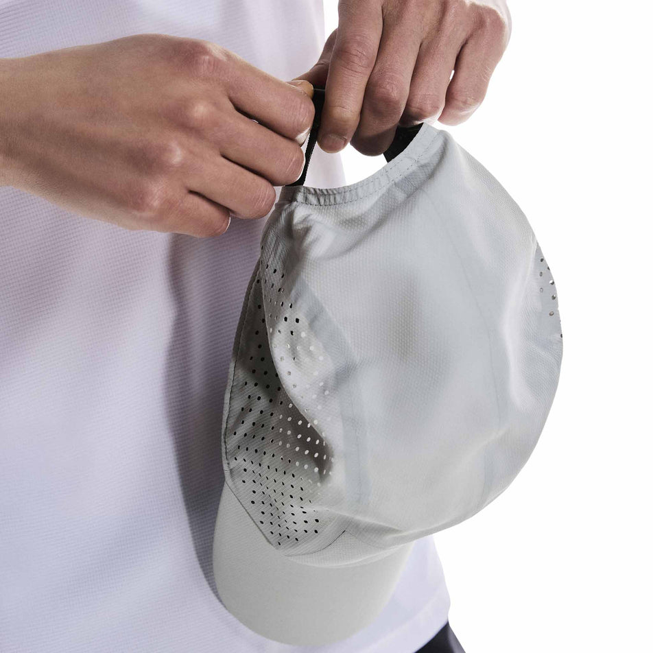 A model adjusting the strap on the back of On Unisex Lightweight Cap in the Glacier colourway. (8583176519842)