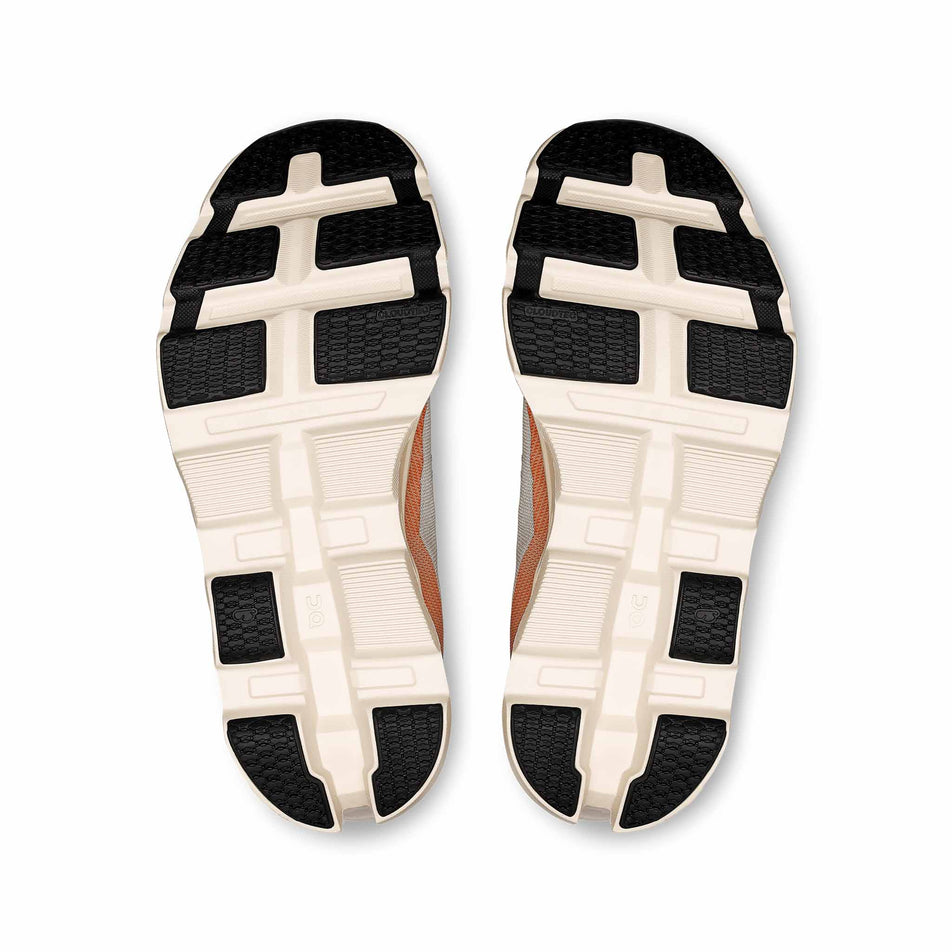 The outsoles of a pair of On Women's Cloudmonster 2 Running Shoes in the Ivory/Tangerine colourway. (8714534453410)