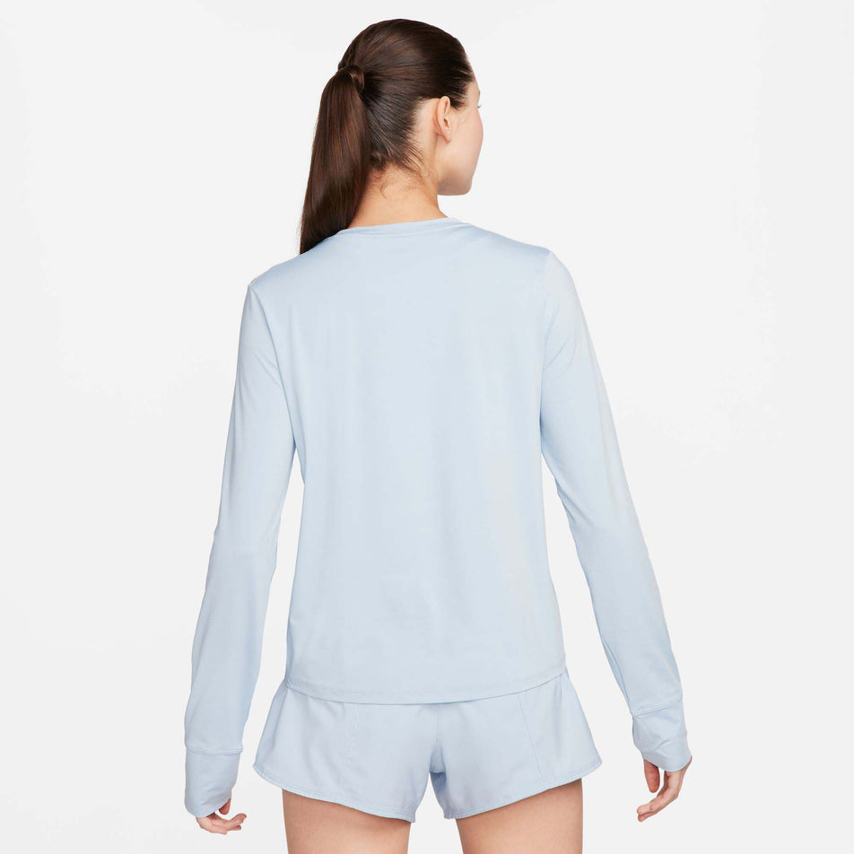 Back view of a model wearing a Nike Women's One Classic Dri-FIT Long-Sleeve Top in the Lt Armory Blue/Black colourway. Model is also wearing Nike shorts. (8157779361954)
