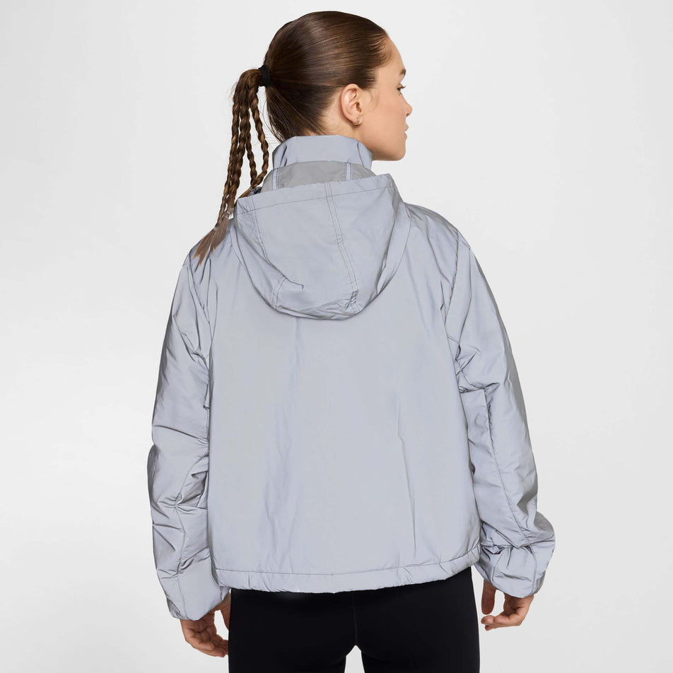 Back view of a model wearing Nike Women's Running Division Therma-FIT Reflective Running Jacket in the Black/Reflective Silv/Refblk colourway. Model is also wearing black Nike tights. (8497648730274)