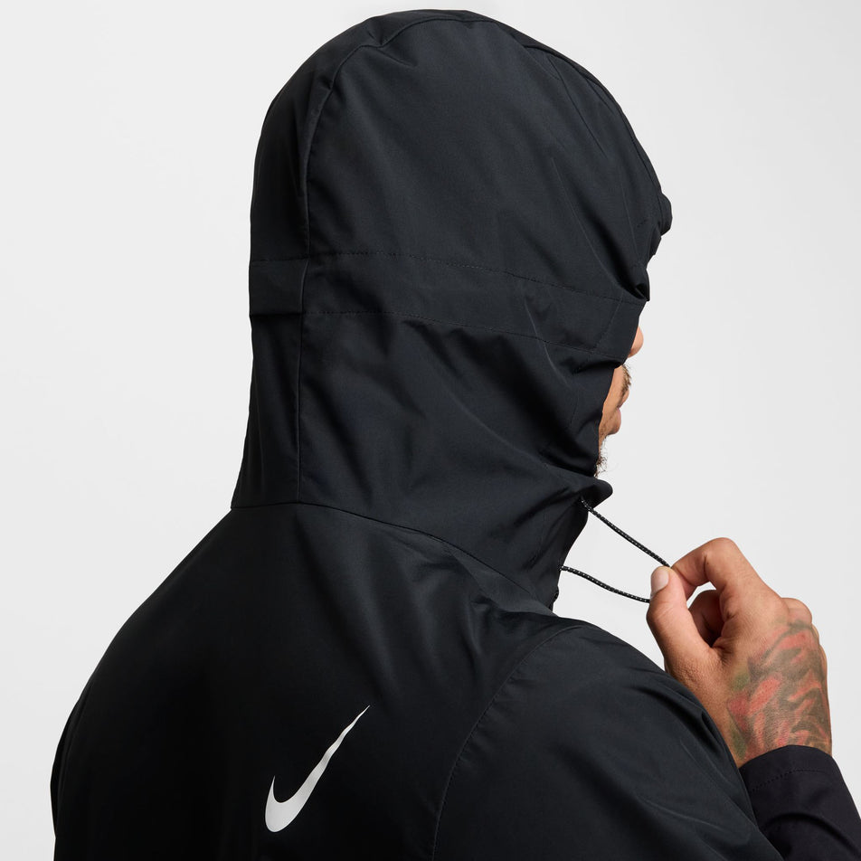 Angled view of a model wearing the Nike Men's AeroSwift Storm-FIT Aerogami Running Jacket in the Black/Summit White colourway with the hood up.