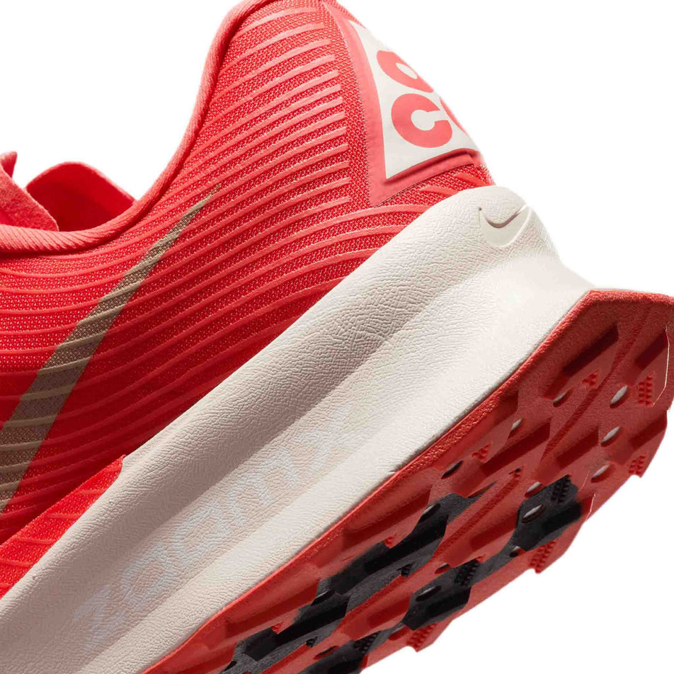Close-up view of the rearfoot section of the left shoe from a pair of Nike Unisex ACG Ultrafly Trail Racing Shoes in the Light Crimson/Pure Platinum-Summit White colourway.