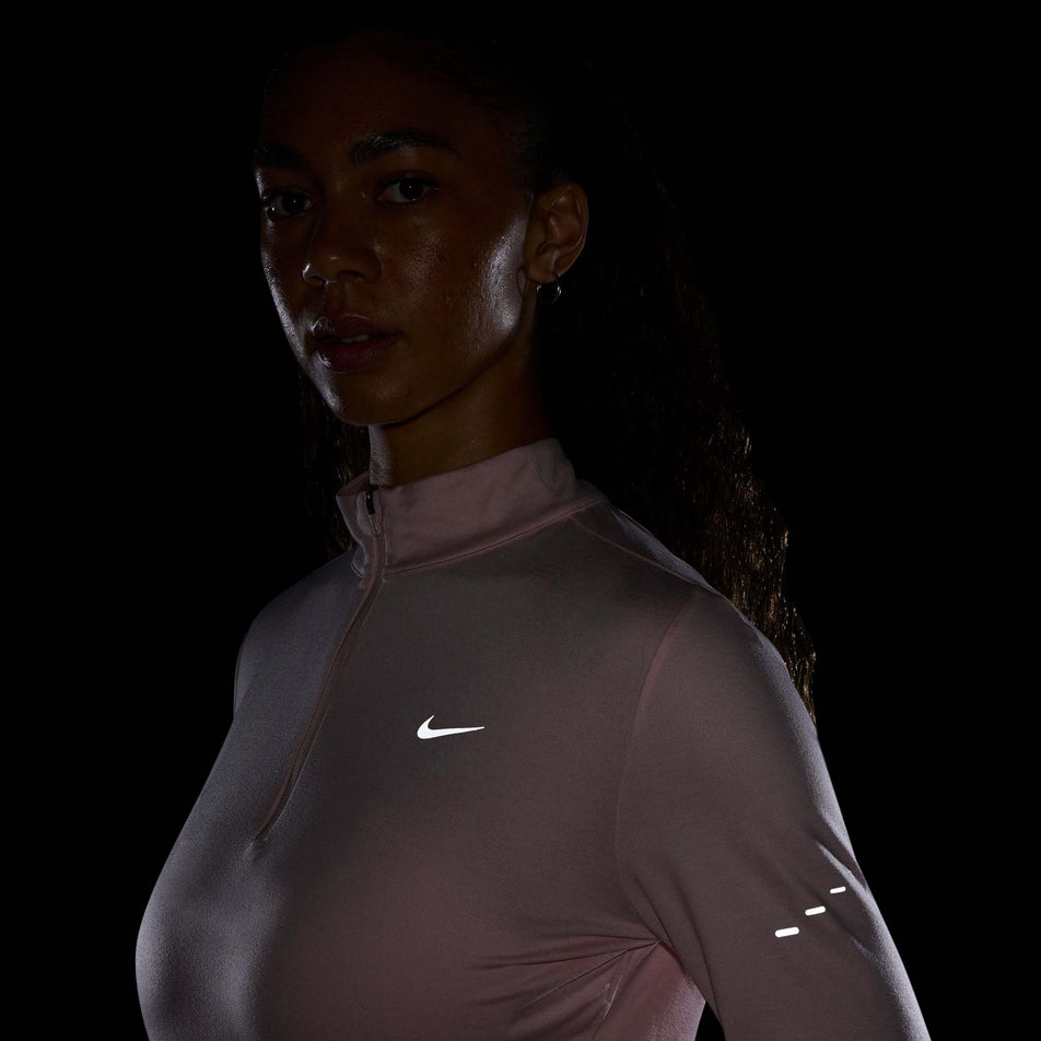 The reflective Swoosh on the front of the Nike Women's Swift Dri-FIT UV 1/4-Zip Long Sleeve Running Top in the Atmosphere/Heather/Reflective Silver colourway. (8621654081698)