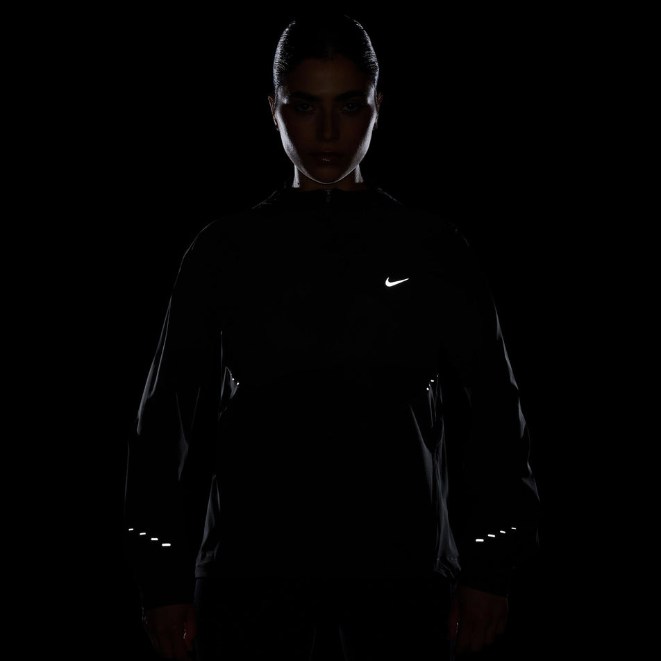 The reflective Nike SWOOSH and reflective graphics on a Nike Women's Swift Repel Packable Running Jacket in the Black/Reflective Silver colourway. (8560817635490)