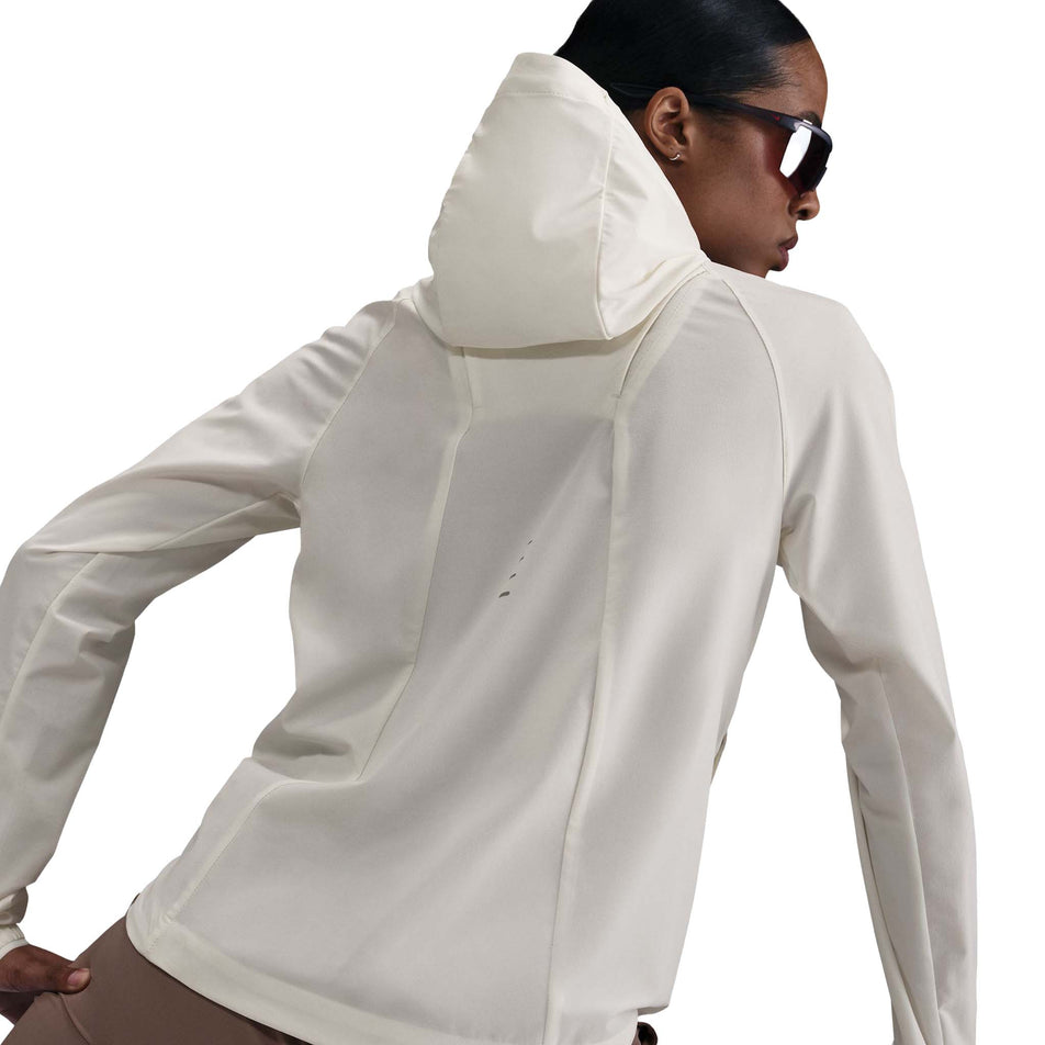 Back view of a model wearing the Nike Women's Swift Repel Packable Running Jacket in the Sail/Reflective Silver colourway. (8732499738786)