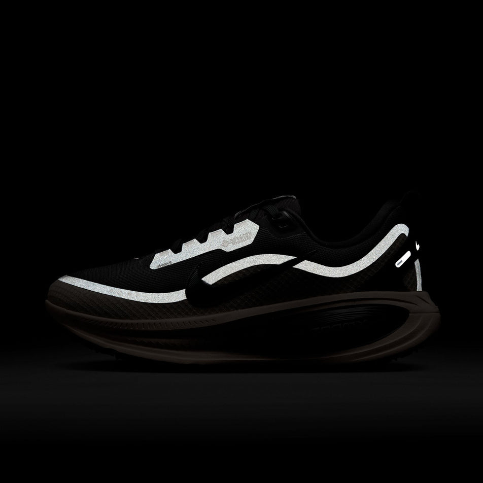 The reflective details on the lateral side of the left shoe from a pair of Nike Women's Vomero 18 GORE-TEX Road Running Shoes in the Black/Black-Crimson Tint-Black colourway. (8756162494626)