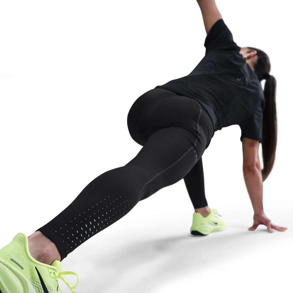 Angled view of a model wearing the Nike Women's Swift High-Waisted 7/8 Running Leggings in the Black/Dark Smoke Grey colourway. (8756531626146)