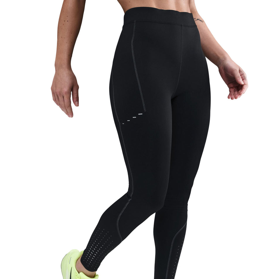 Angled view of a model wearing the Nike Women's Swift High-Waisted 7/8 Running Leggings in the Black/Dark Smoke Grey colourway. (8756531626146)