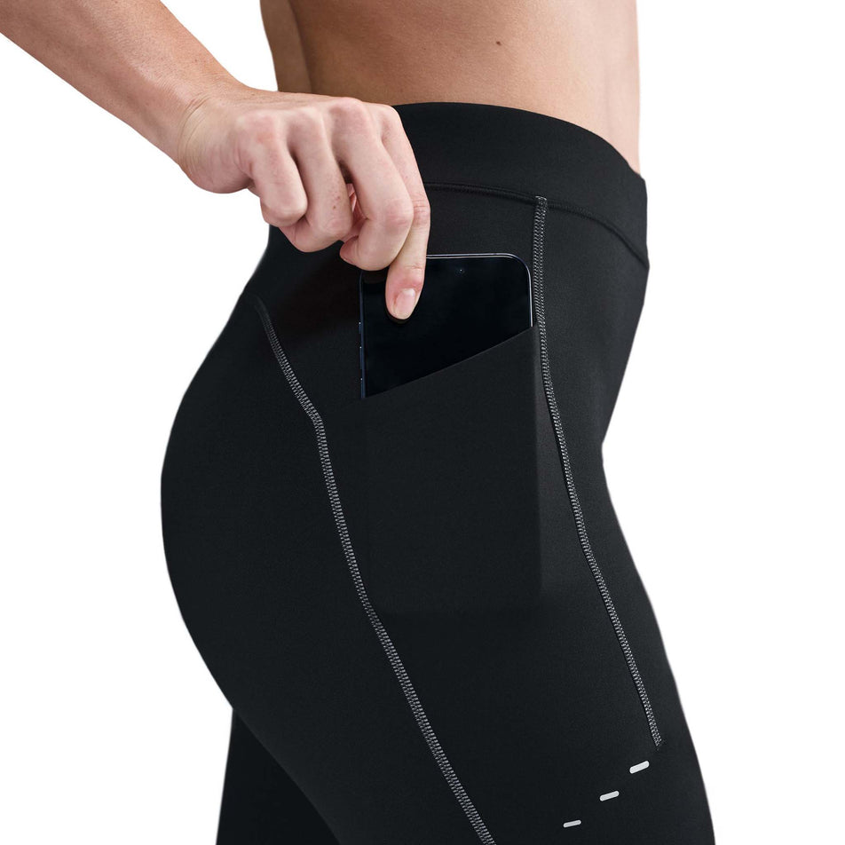 A model demonstrating the drop-in pocket on the side of the Nike Women's Swift High-Waisted 7/8 Running Leggings in the Black/Dark Smoke Grey colourway. (8756531626146)