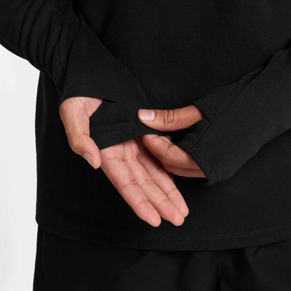 A model demonstrating the thumb loop on the sleeve of the Nike Men's Dri-FIT Stride Running Waffle Crew in the Black/Reflective Silver colourway. (8733246980258)