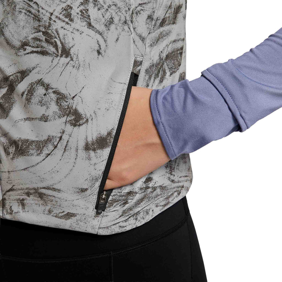 A model demonstrating one of the zippered pockets on the Nike Women's Therma-FIT ADV Reflective Running Vest in the Vast Grey/Black colourway. (8756535394466)
