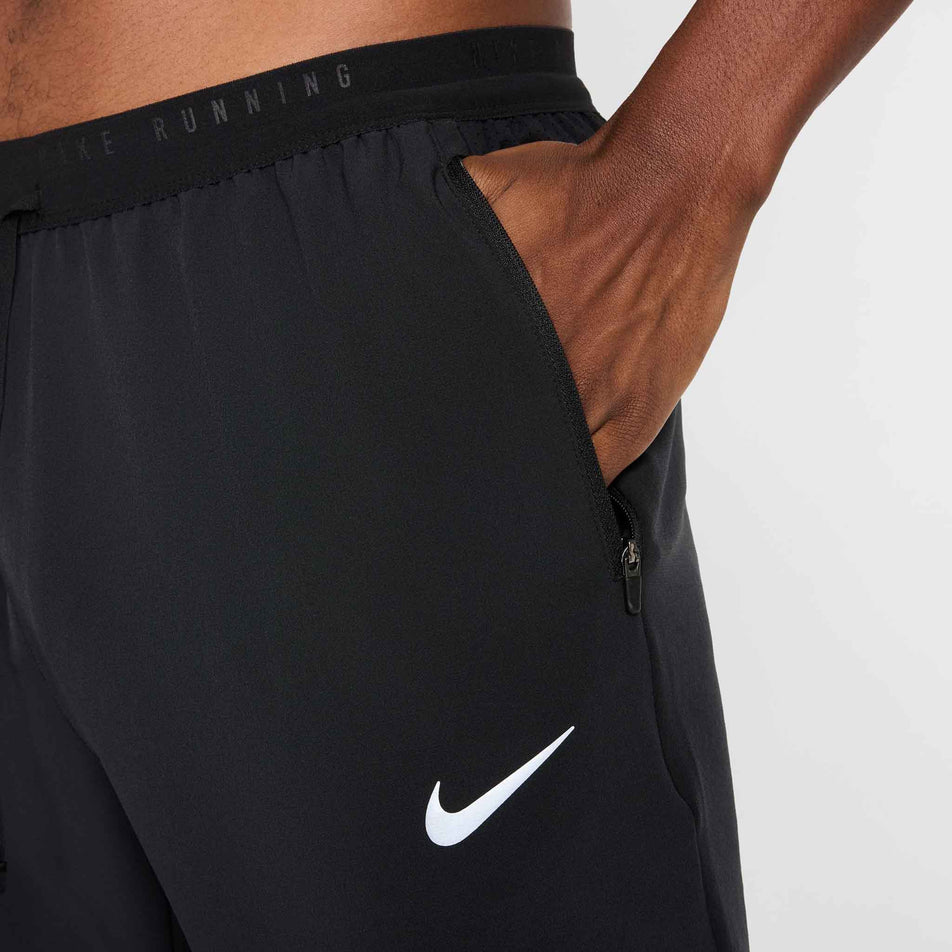 A model demonstrating the zip pocket on the side of the Nike Men's Stride Dri-FIT Woven Running Pants in the Black/Reflective Silver colourway. (8778202644642)