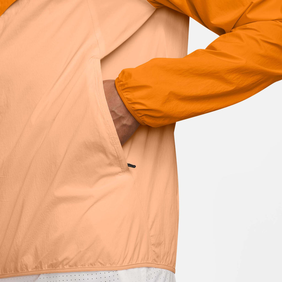 A model demonstrating the zippered side pocket on the Nike Men's Stride Repel UV Running Jacket in the Bright Ceramic/Reflective Silver colourway. (8778203693218)