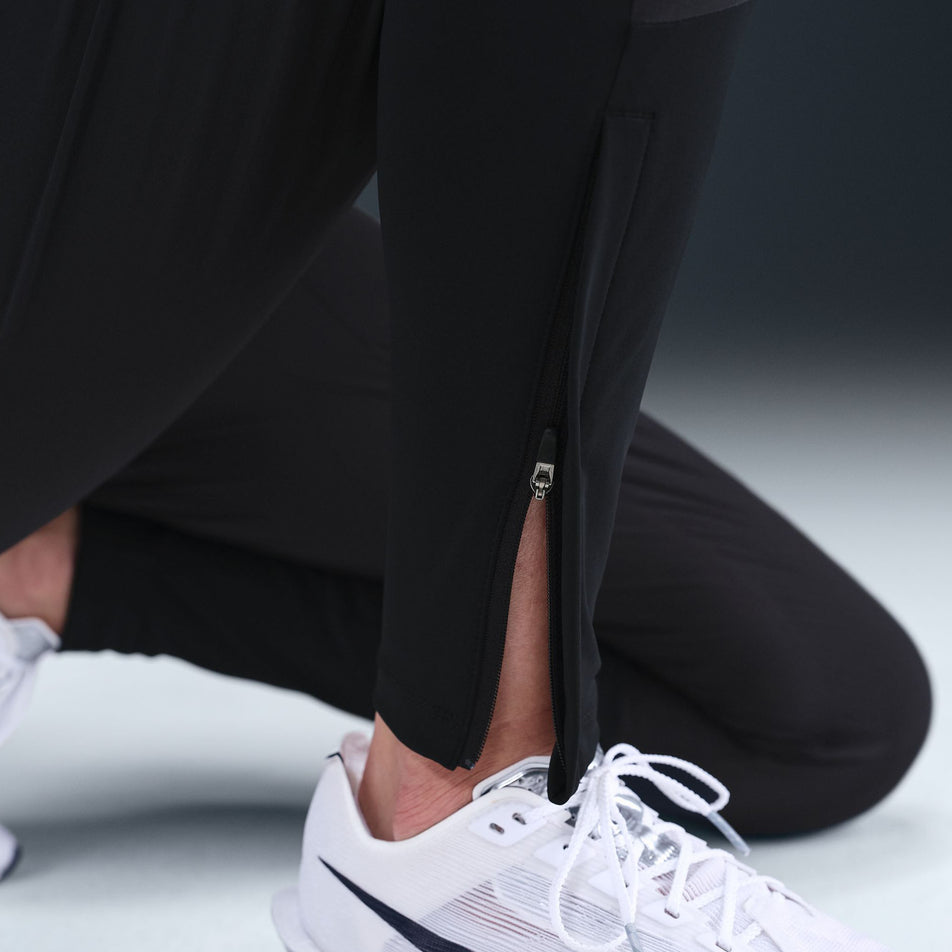Close-up of the ankle zip on the Nike Women's Dri-FIT Mid-Rise Running Pants in the Black/Reflective Silver colourway. (8732466151586)