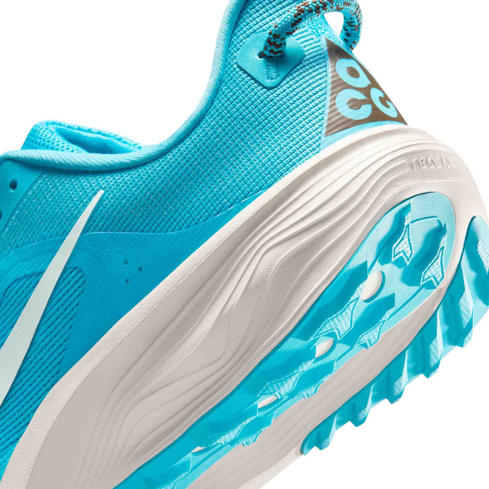 Close-up view of the rearfoot section of the left shoe from a pair of Nike Men's ACG Pegasus Trail Running Shoes in the Baltic Blue/Summit White-Light Orewood Brown colourway.