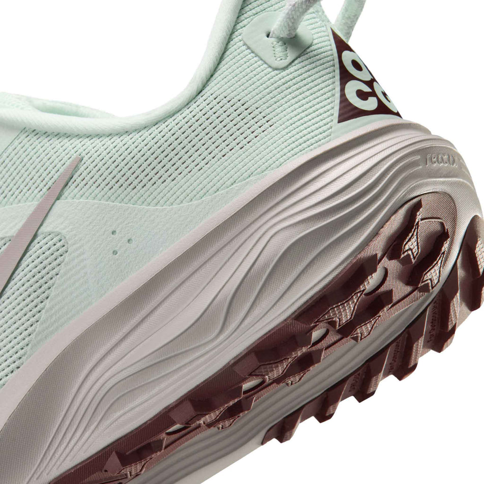 Close-up view of the rearfoot section of the left shoe from a pair of Nike Women's ACG Pegasus Trail Running Shoes in the Barely Green/Silver Lilac-Light Bone colourway.