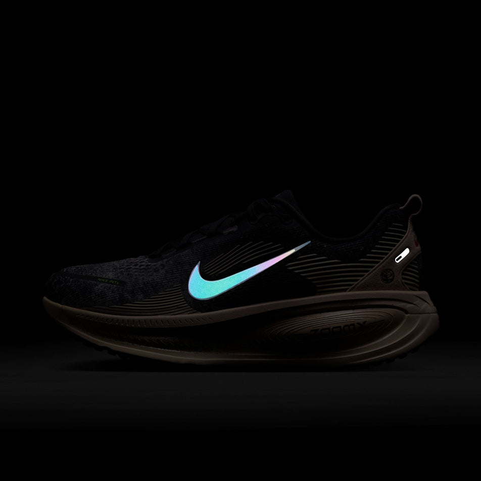 The reflective Nike Swoosh on the lateral side of the left shoe from a pair of Nike Men's Vomero 18 Road Running Shoes in the Oatmeal/Black-Anthracite-Volt colourway. (8684581552290)