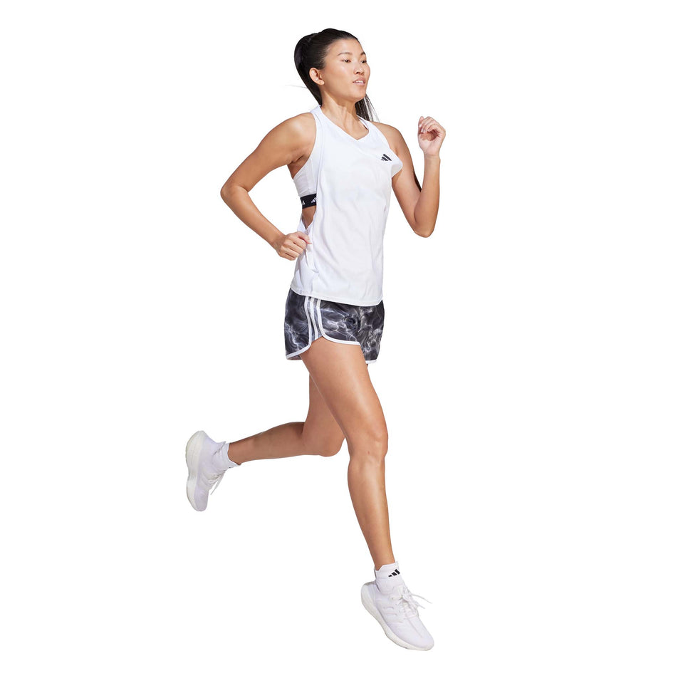Front side view of a model wearing a pair of adidas Women's Marathon 20 Allover Print Shorts in the White/Black/Grey Six colourway. Model is in a running pose.  (8005354291362)