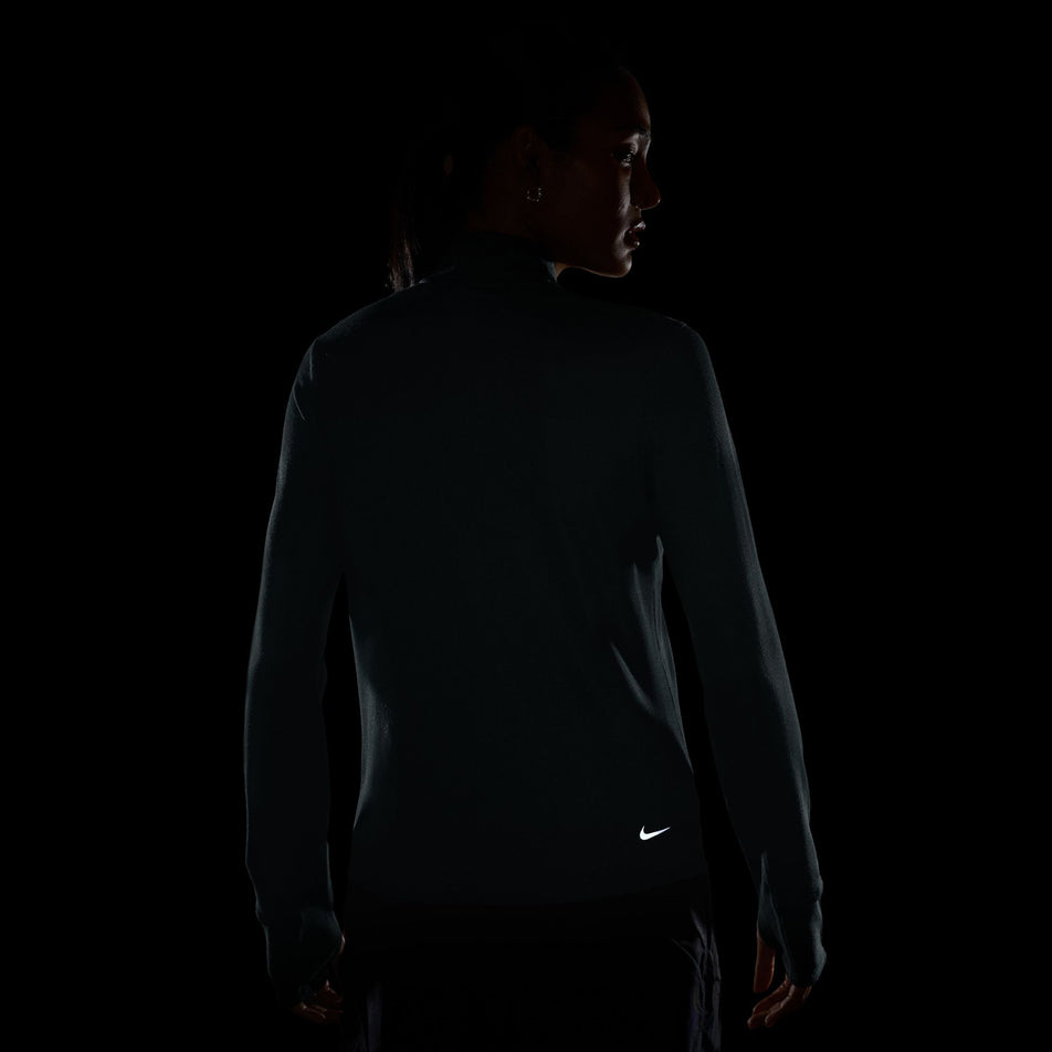 The reflective swoosh on the back of the Nike Women's ACG Dri-FIT 1/2-Zip Trail Running Top in the Mineral Slate/Summit White colourway.