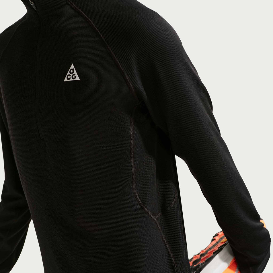 Angled view of a model wearing the Nike Men's ACG Dri-FIT Mid-Layer 1/4-Zip Trail Running Top in the Black/Black/Summit White colourway.