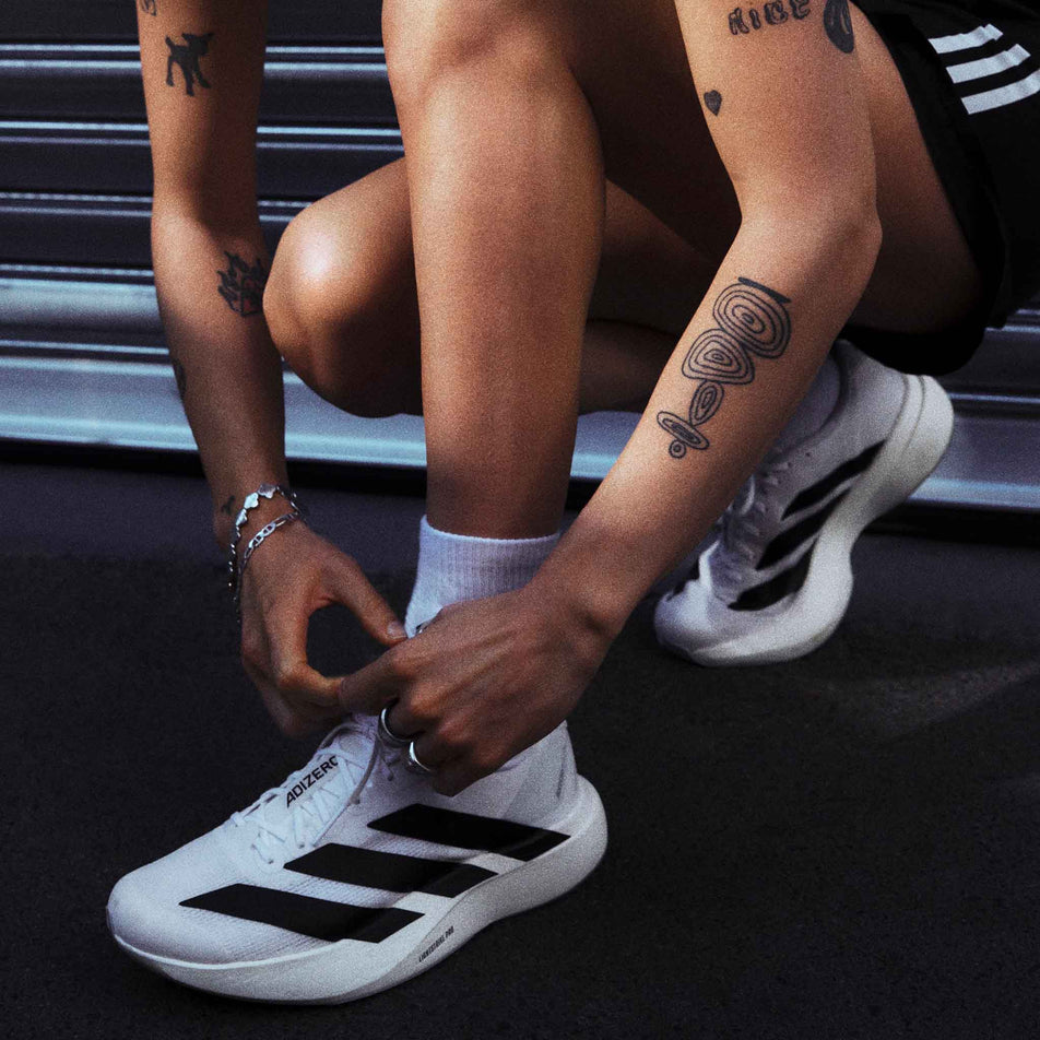 A model wearing a pair of adidas Women's Adizero EVO SL Running Shoes in the Ftwr White/Core Black/Ftwr White colourway.
