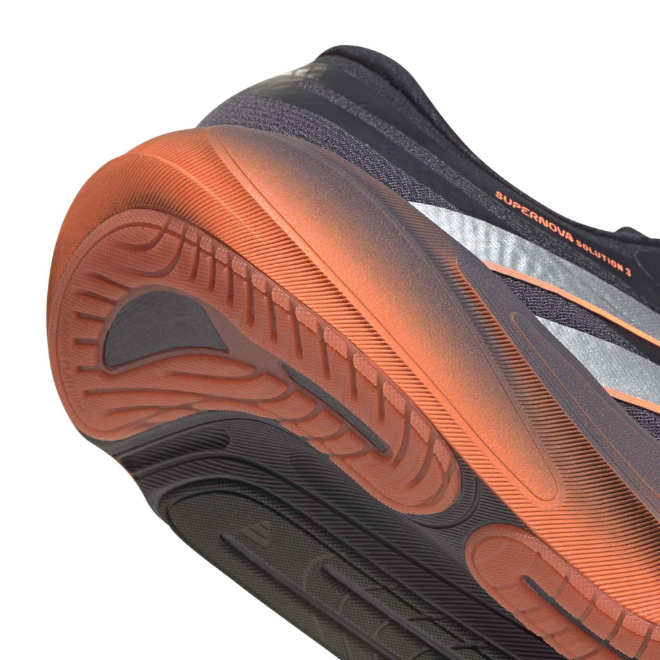 Close-up view of the rearfoot section of the right shoe from a pair of adidas Men's Supernova Solution 3 Running Shoes in the Aurora Onix/Silver met./Lucid Orange colourway.